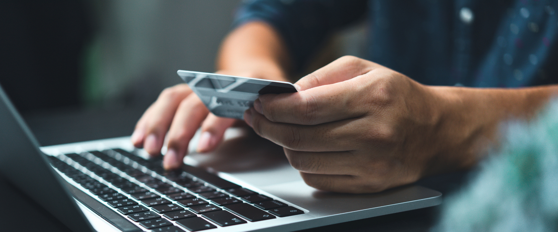 Man holding a credit card and typing in details on the laptop.